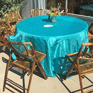 Bamboo Chairs surrounding a round table covered with a turquoise pin tuck tablecloth.