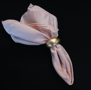 Close up of a blush rose colored napkin in a gold napkin ring.