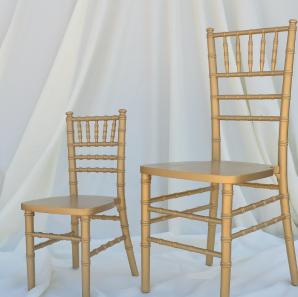 Kids gold Chiavari chair placed next to an normal sized gold Chiavair chair in front of  a white backdrop.